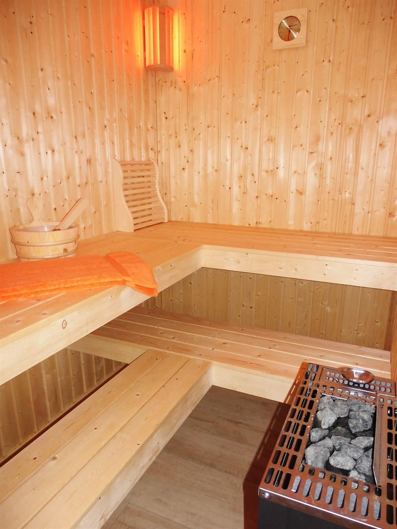 Sauna aus hellem Holz mit zwei Liegebänken und Saunaofen
